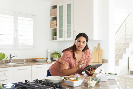 Young plus size biracial woman browses a recipe on a tablet in a home kitchen unaltered - Powered by Adobe
