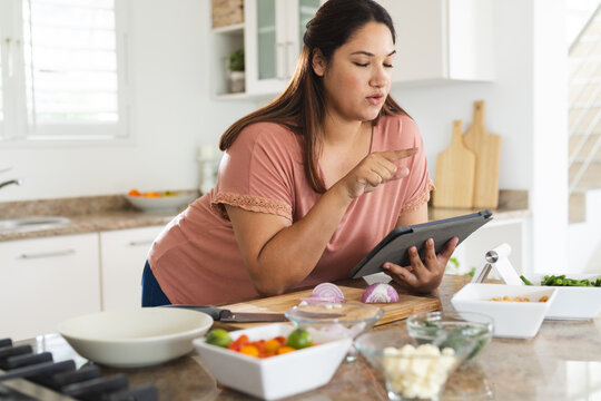 Young plus size biracial woman checks a recipe on her tablet in the kitchen unaltered