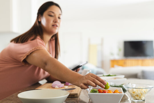 Young plus size biracial woman prepares a salad in a home kitchen - Powered by Adobe