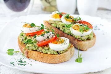Fototapeta na wymiar Delicious toast with avocado, boiled egg, tomatoes and microgreen on a white plate. Healthy eating, breakfast. Keto diet food. Trendy food.