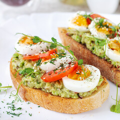 Delicious toast with avocado, boiled egg, tomatoes and microgreen on a white plate. Healthy eating, breakfast. Keto diet food. Trendy food.