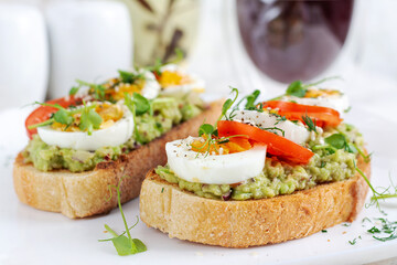 Delicious toast with avocado, boiled egg, tomatoes and microgreen on a white plate. Healthy eating,...