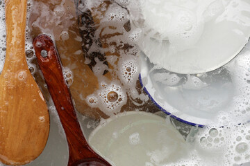 Wooden spoon, and dishes in water and bubbles of dishwashing liquid