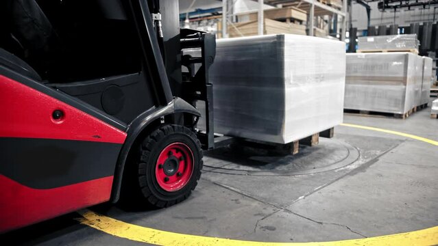 Logistics employee drive a forklift containing stacked cargo boxes or packages and slowly pickup box on the floor.