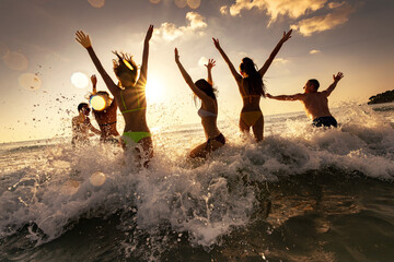 Large group of happy young friends of tourists are having fun, runs and jumps at sunset sea beach....