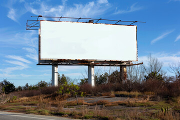 An empty billboard stands tall beside a deserted mountain road, offering a blank canvas against a rugged natural landscape.