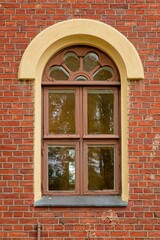 Brown painted framed window with arch on a red brick wall.