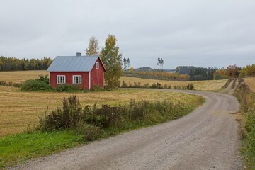 Old traditional red painted house in countryside and gravel road.