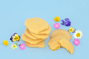 Homemade white chocolate custard cookies with scattered Spring flowers and wildflowers on blue background. Natural comfort food floral nature composition.