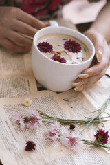 Female hands holding a cup of cappuccino with flowers on a book background