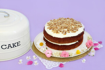 Carrot and walnut cake for birthday party with summer flowers and cake tin cover on purple...