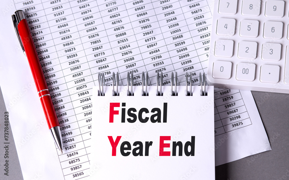 Aufkleber fiscal year end text on notebook with pen, calculator and chart on grey background