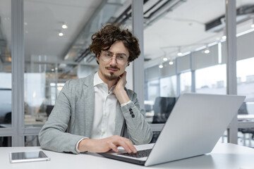 Portrait of a contemplative young businessman with curly hair working diligently on his laptop in a modern office setting.