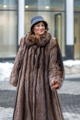 A stylish middle-aged woman in a fur coat and hat on a city street during the Christmas holidays