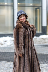 A stylish middle-aged woman in a fur coat and hat on a city street during the Christmas holidays