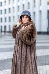 A stylish middle-aged woman in a fur coat and hat on a city street during the Christmas holidays