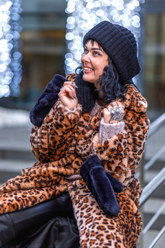 A stylish young woman in a leopard print fur coat and on the street of the city during the Christmas holidays