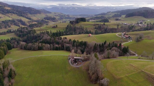 Drone flight over a hilly landscape in a cloudy weather with mountains in the background
