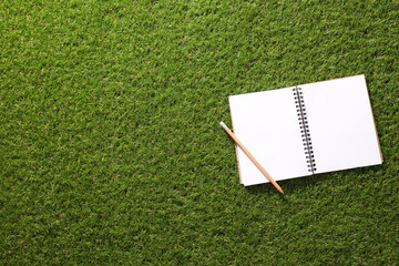 A paper notebook with a pencil on the grass.