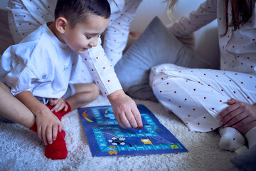 mother with teenage daughter and little son in pajamas playing board games on the floor