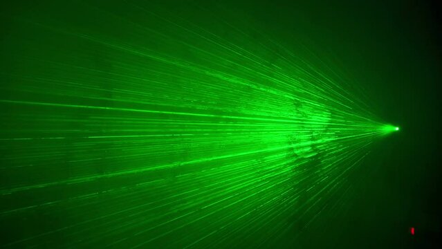 Green laser rays lighting in smoke on a dark background. Laser disco stripe beams shine in fog. Intense bright power lasers cutting through darkness. Concept of science, disco, party, researching