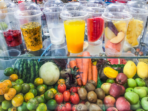 Colorful display of fresh fruits and ready-to-drink fruit juices in clear plastic cups, promoting healthy lifestyle choices..