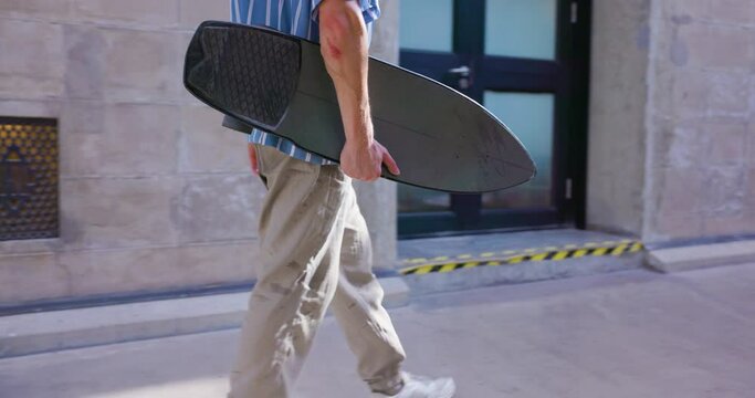 Urban skater holding skateboard walking around the city.