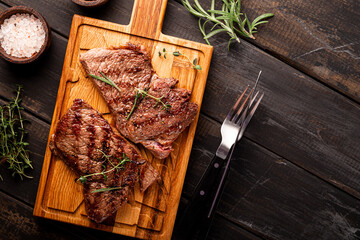 Grilled beef steak, well done with seasons and green on a black wooden background top view, copy...