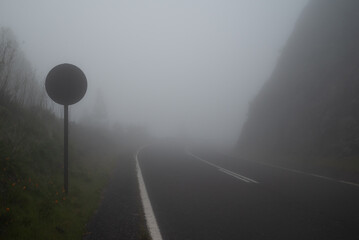 Foggy mountain road with a curve and a round street sign of speed limit