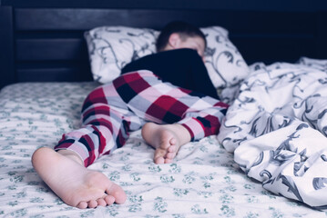 Bare feet of a child. A child in pajamas. Bare feet sticking out from under the blankets. The boy is sleeping in bed. Foot and leg - obrazy, fototapety, plakaty