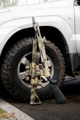 A shotgun and a rifle gun standing against the wheel of a silver SUV