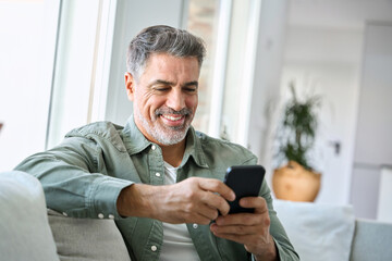 Smiling happy senior mature middle aged man holding cell mobile phone using smartphone sitting at...