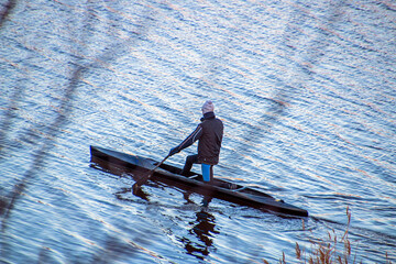 A rower with an oar in his hands floats a kayak in the distance on a lake in autumn