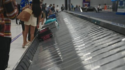 A woman is rolling a suitcase on a moving airport conveyor belt