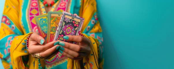 Fotobehang Woman holding  tarot and oracle cards, on turquoise background, inviting users to seek guidance, self-reflection, and spiritual insights. These cards serve as powerful tools for divination. © Holly Berridge