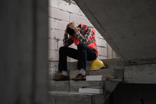 Young Asian male construction worker staff feeling sad and upset while sitting on the floor of the building construction site due to been fired from job cause by company bankruptcy economic recession.