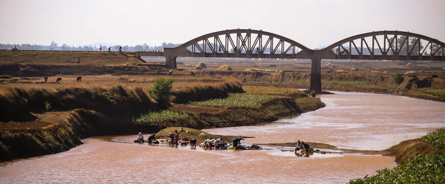 malgasy people do their laundy in a river with an arch bridge in background