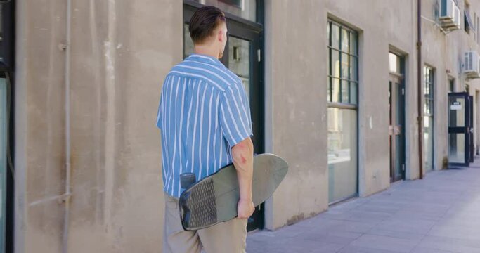 Urban skater holding skateboard walking around the city.