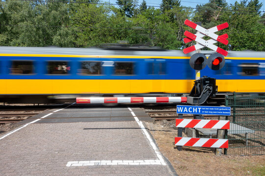 Treinstel van de Nederlandse Spoorwegen passeert een bewaakte spoorwegovergang die beveiligt is met een enkele slagboom en knipperlicht