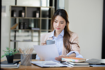 Happy asian young businesswoman using laptop with business finance chart sitting at office working space, Business finance and accounting woman concept.