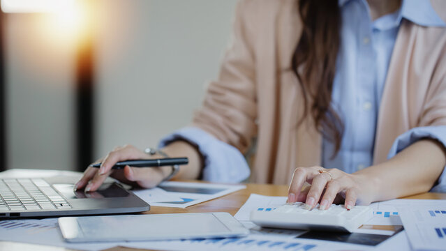 Happy asian young businesswoman using laptop with business finance chart sitting at office working space, Business finance and accounting woman concept.