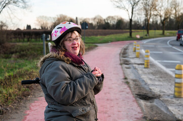 Happy 41 yo white woman with the Down Syndrome, standing at a cycling path, Belgium
