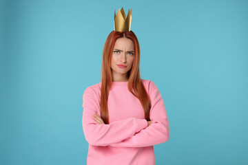 Emotional young woman with princess crown on light blue background © New Africa