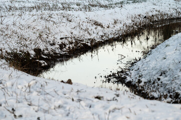 The bending Molenbeek creek through the snowy meadows in Jette, Belgium