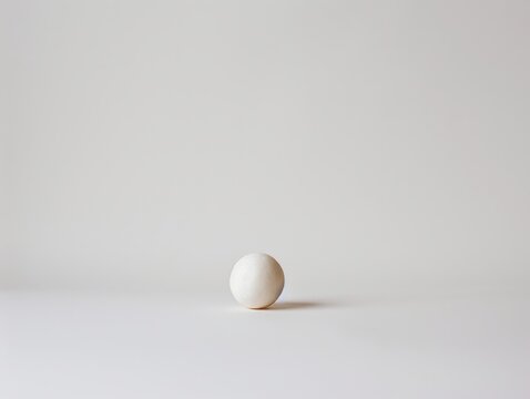 A small spherical ball of ceramic isolated in a white room, a metaphorical art, no pun intended, a genuine art. Created with Generative AI.