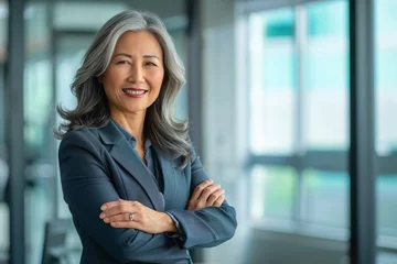 Fotobehang Happy proud prosperous mid aged mature professional Asian business woman ceo executive wearing suit standing in office arms crossed © Danko