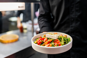 Men's chef or waiter hands hold a cheese salad with vegetables on plate