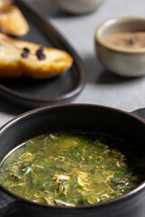 Soup with green sorrel in black ceramic pot on gray background