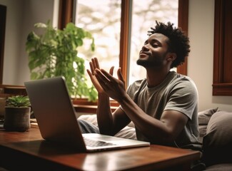 Man in gratitude pose with laptop at home.
