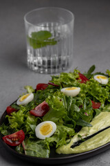 Fresh green salad with quail eggs, cherry tomatoes and guacamole in black plate on grey background